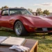 Red classic Chevrolet Corvette displayed on grass at an outdoor car show, with a small placard in front and an open documentation binder on a nearby table in the foreground.